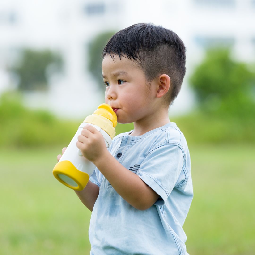enfant asiatique qui boit dans une gourde avec paille jaune dans un parc