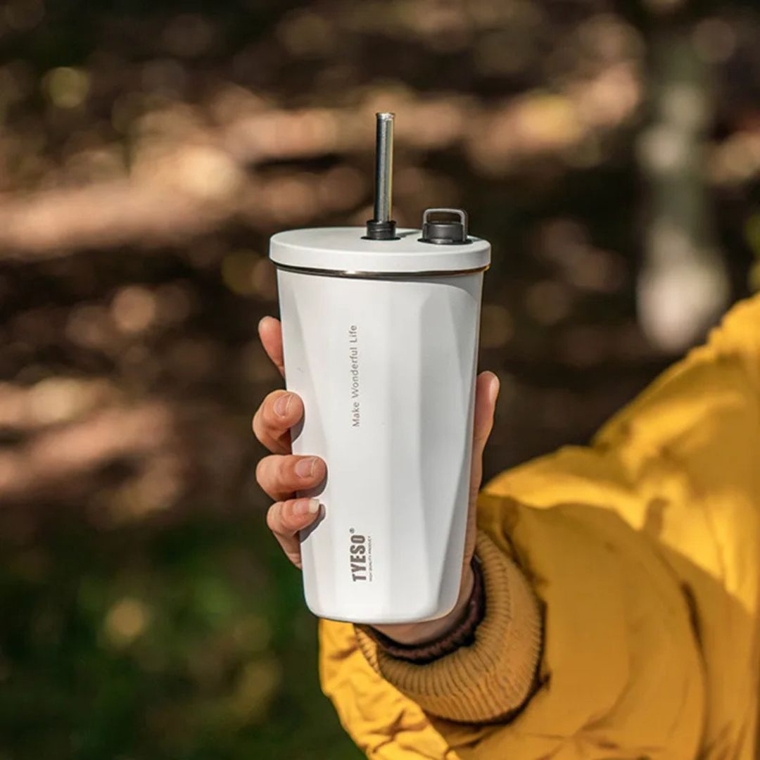 gourde avec paille isotherme tenu dans la main d'une personne en mentaux jaune dans une forêt